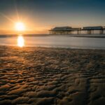 Spiaggia affollata con turisti, palme e acque cristalline, simbolo della popolarità crescente della località di mare.