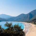 Spiaggia soleggiata in Grecia con ombrelloni e turisti, ideale per una vacanza low cost a maggio.