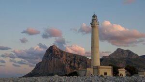 Faro isolato su un promontorio, circondato da natura, ideale per un trekking panoramico in Italia.