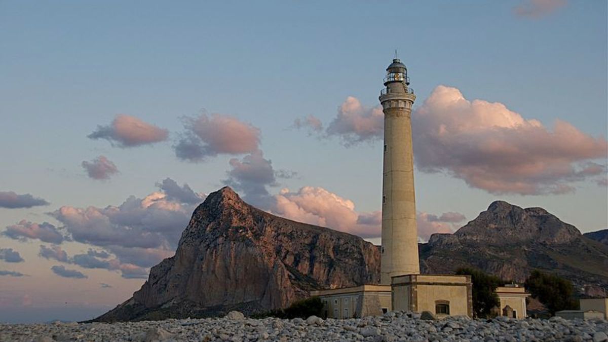 Faro isolato su un promontorio, circondato da natura, ideale per un trekking panoramico in Italia.