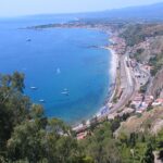 Panorama mozzafiato di una spiaggia siciliana con mare cristallino e scogliere.
